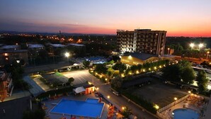 A hotel with multiple swimming pools, a parking lot, and a large building with illuminated windows. - Hotel Avila In (Rimini)