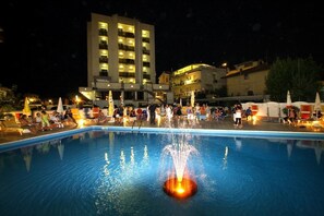 A swimming pool with a fountain feature, surrounded by lounge chairs and umbrellas. - Hotel Avila In (Rimini)