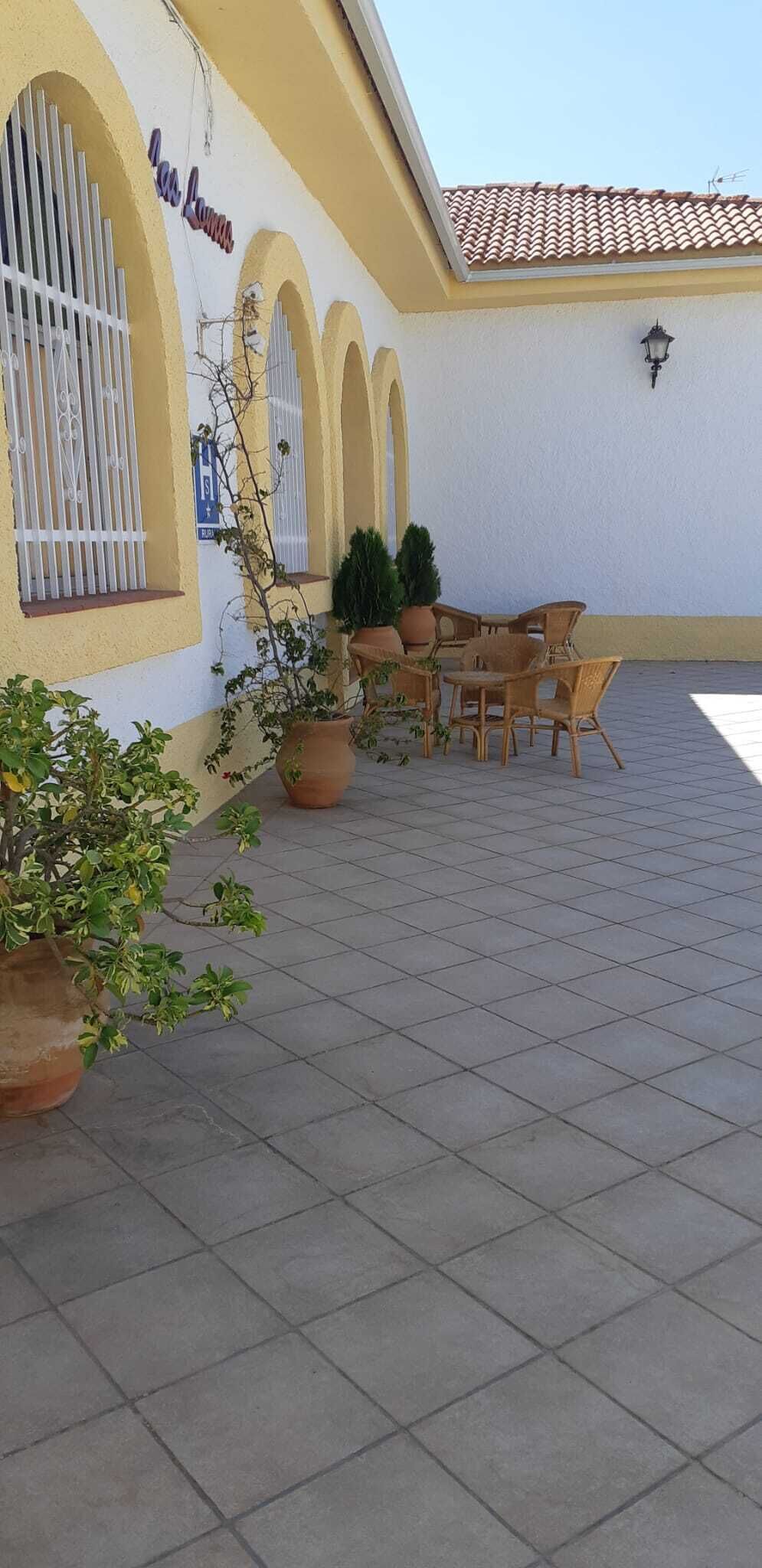 Un patio al aire libre con un edificio amarillo, piso de baldosas y un conjunto de mesas y sillas.