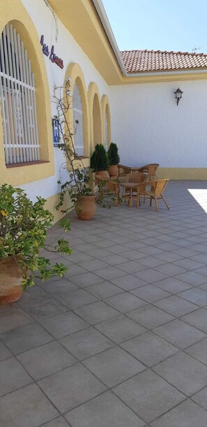 Un patio al aire libre con un edificio amarillo, piso de baldosas y un conjunto de mesas y sillas.