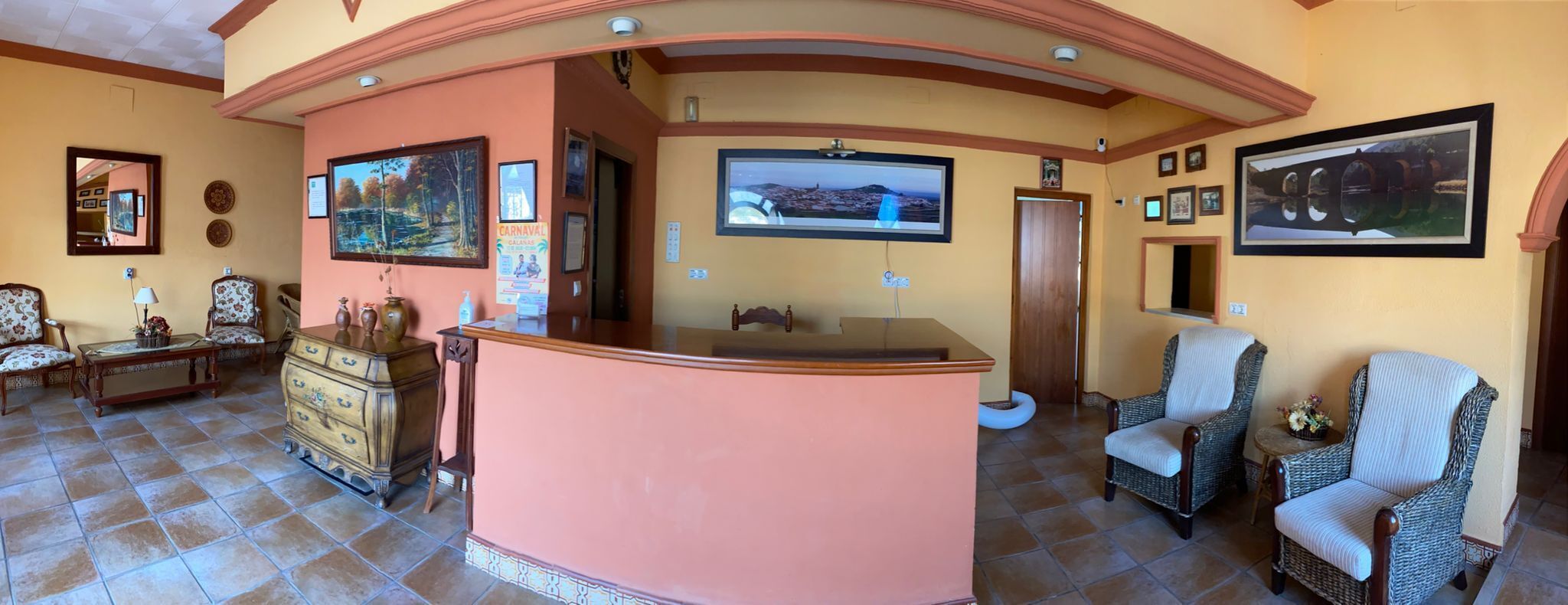 A reception area with a wooden counter, two wicker chairs, a sofa, and a television mounted on the wall.