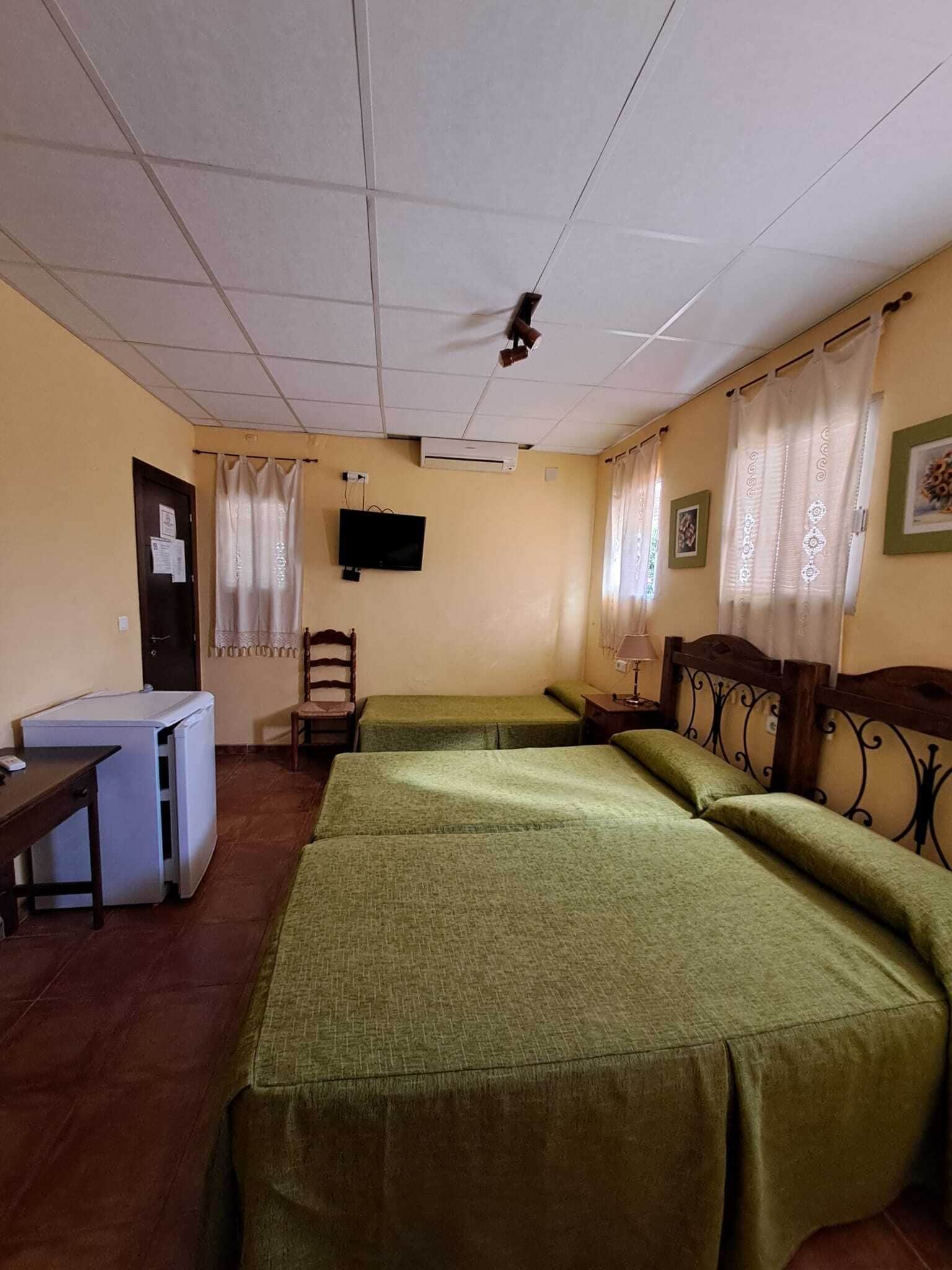 A room with two beds, a desk, a chair, a television, and a window with curtains.