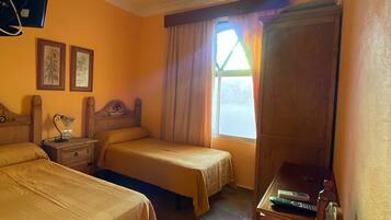 Quarto de hotel com duas camas, uma escrivaninha, uma cadeira, uma televisão e uma janela com cortinas.