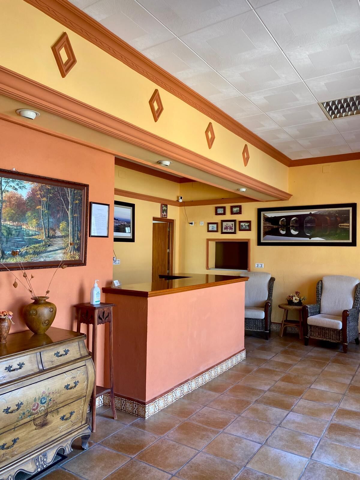 Una zona de recepción con un mostrador de madera, cuadros en las paredes y un aparador antiguo.