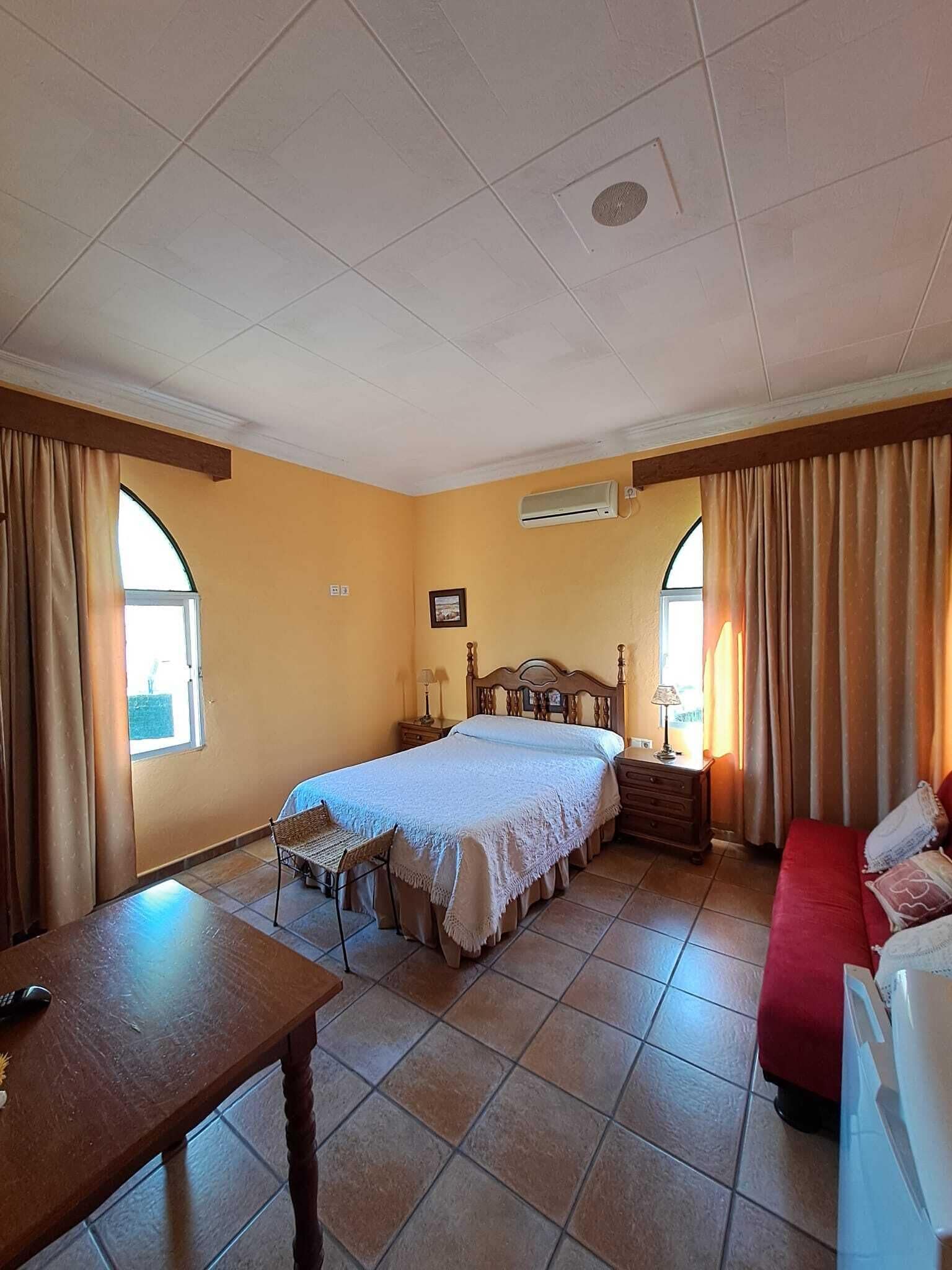 Un dormitorio con una cama, una mesita de noche, una silla, un sofá rojo y una ventana.
