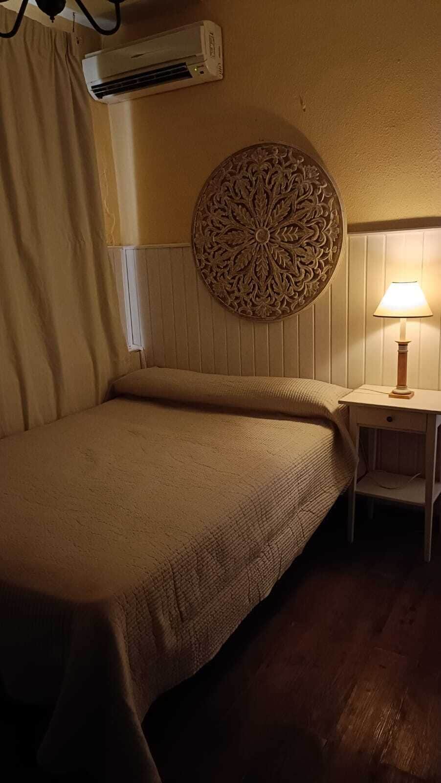 Ein Zimmer mit einem Bett, einer Wand-Klimaanlage, einer Wanddekoration und einer Nachttischlampe.