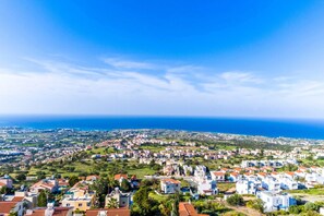 A coastal town with white buildings and red roofs, surrounded by greenery and the sea.