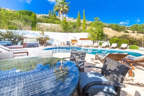 A poolside area with lounge chairs, a glass table, and a barbecue grill.
