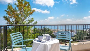 A balcony with two chairs and a table, a view of the sea, and a tree with orange flowers. - Villa Atlantica (Pegeia)