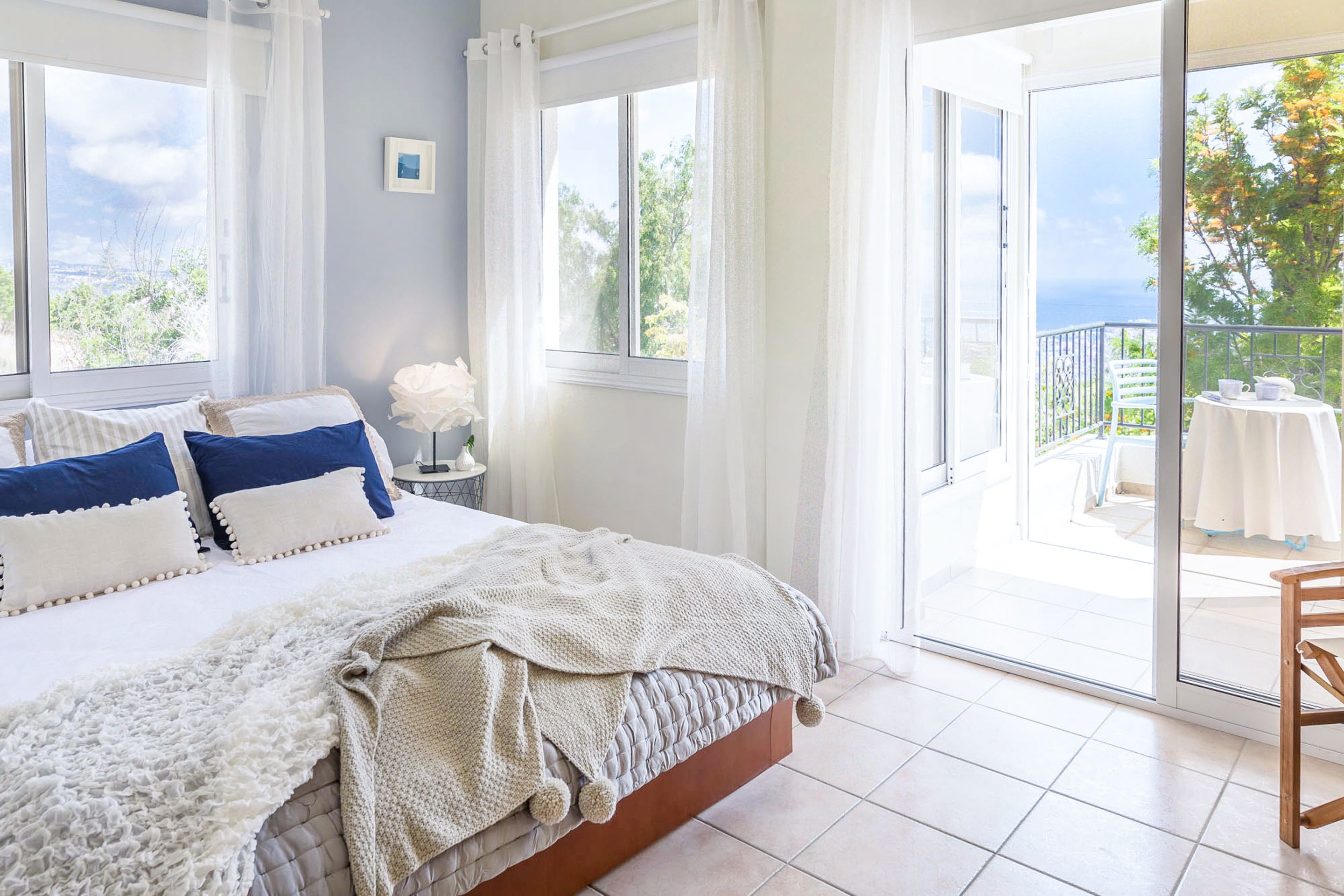Un dormitorio con una cama grande, vistas al exterior y un balcón con una mesa y sillas.