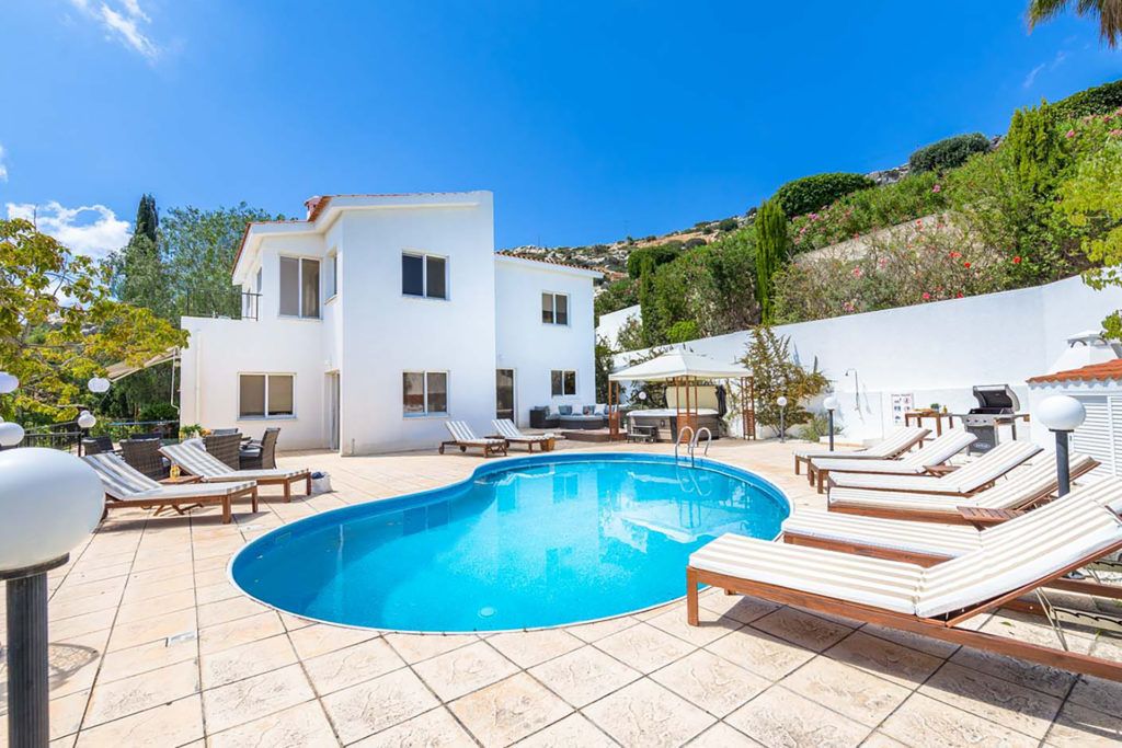 Una villa moderna con piscina, tumbonas y un área de patio.