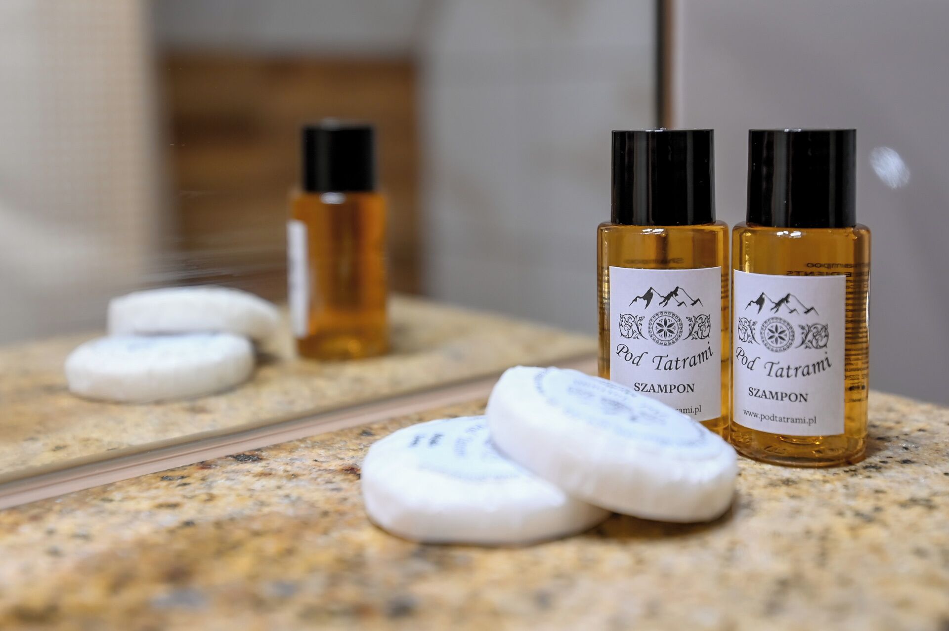 Two bottles of Pod Tatrami shampoo on a granite countertop with a mirror reflecting the bottles and two white soap bars.