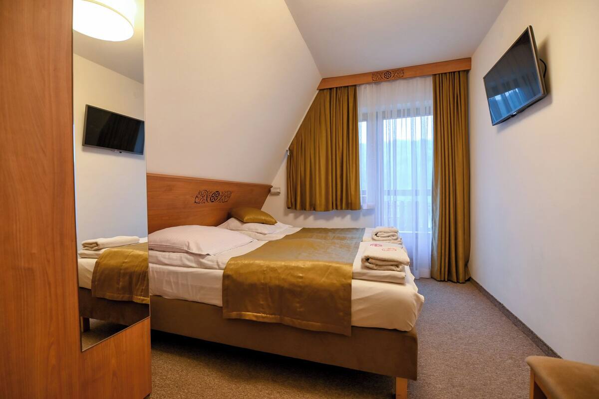 Una habitación de hotel con cama, televisión y ventana con cortinas.