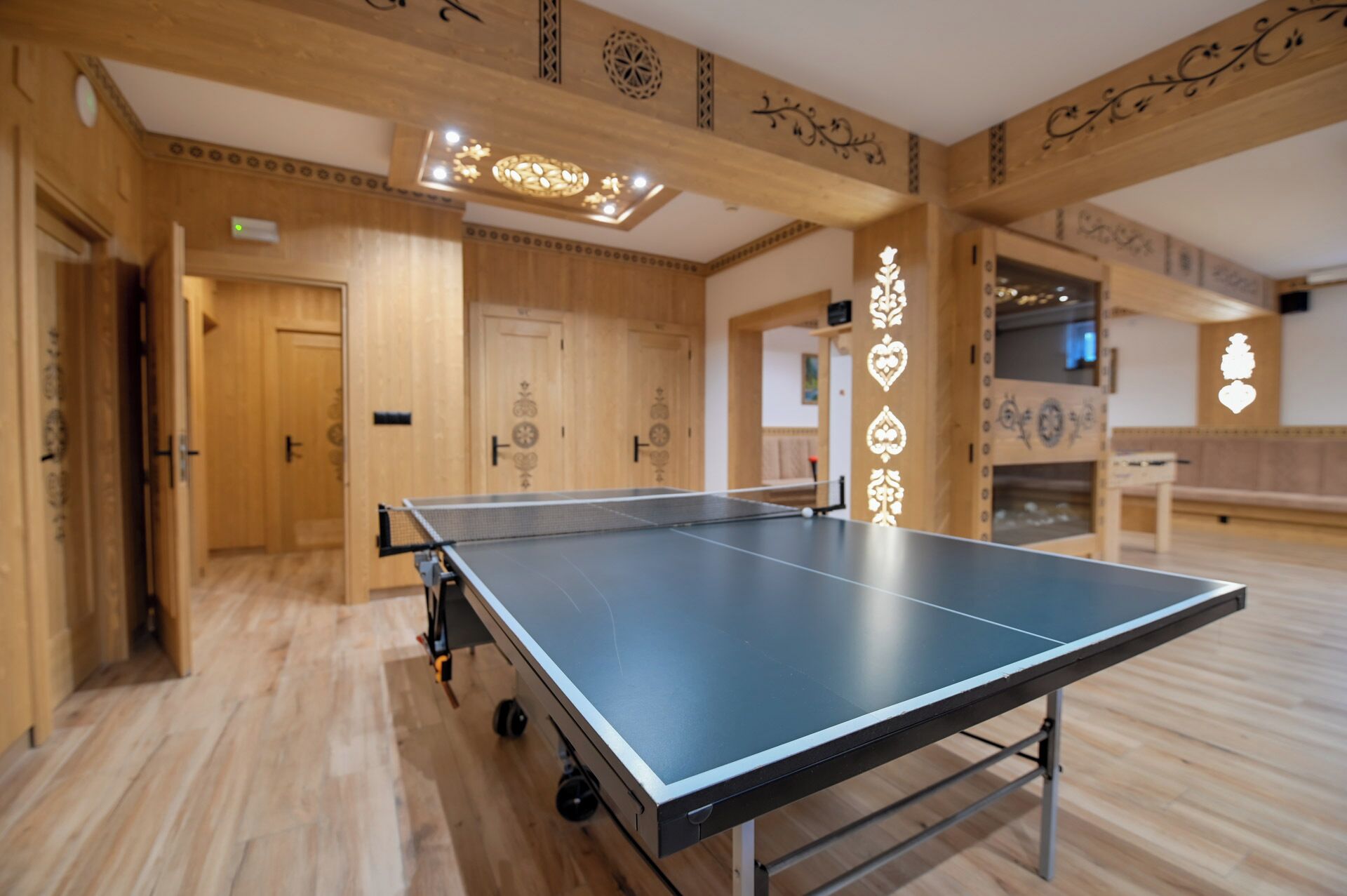 A ping pong table in a room with wooden walls and ceiling, a door, and a small table with a TV.
