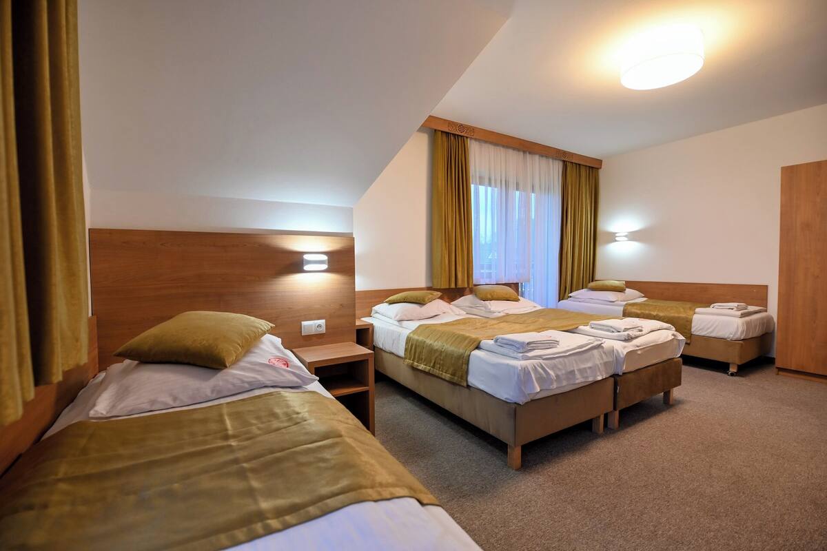 Habitación de hotel con tres camas, cabeceros de madera y una lámpara en el techo.
