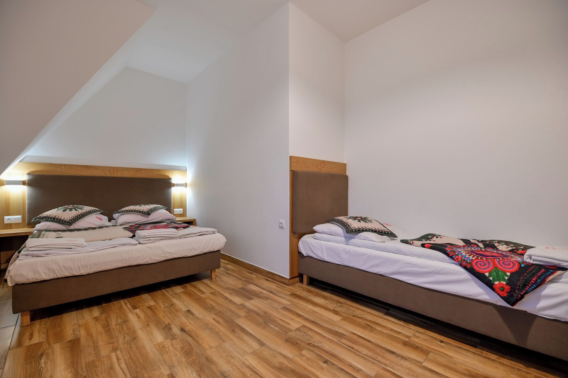 A room with two beds, wooden flooring, and a sloped ceiling.