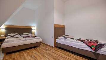 A room with two beds, wooden flooring, and a sloped ceiling.