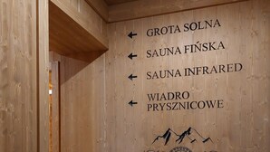 A wooden wall with directional signs for various facilities including 'GROTA SOLNA', 'SAUNA FINSKA', 'SAUNA INFRARED', and 'WIADRO PRYSZNICOWE'. - Pod Tatrami (Bukowina Tatrzanska)