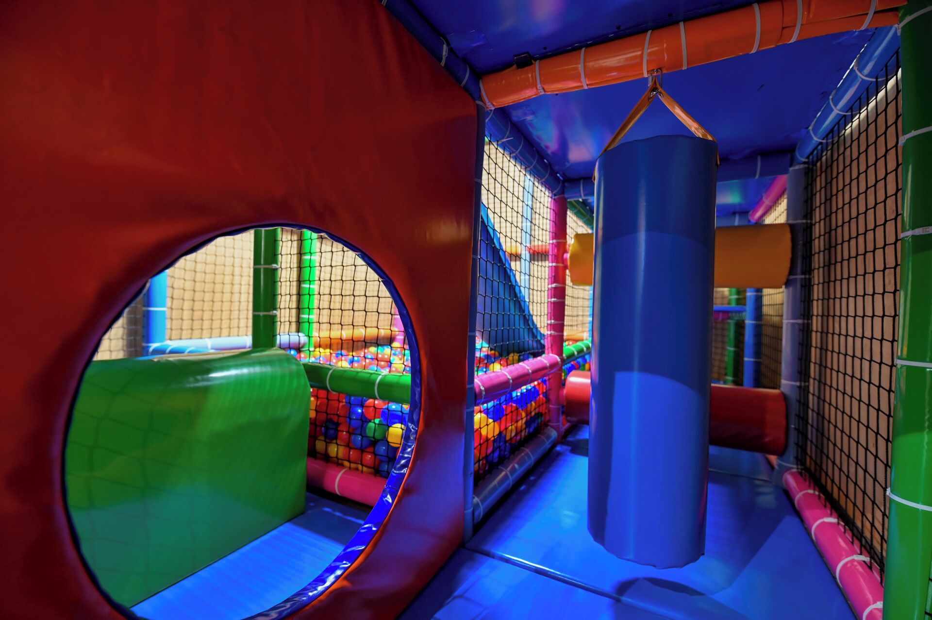 Un espace de jeux comprenant un filet d’escalade, un sac de frappe et des structures colorées.