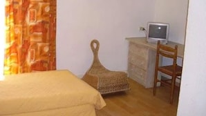 Una habitación con una cama, un escritorio con ordenador, una silla y una cesta de mimbre.