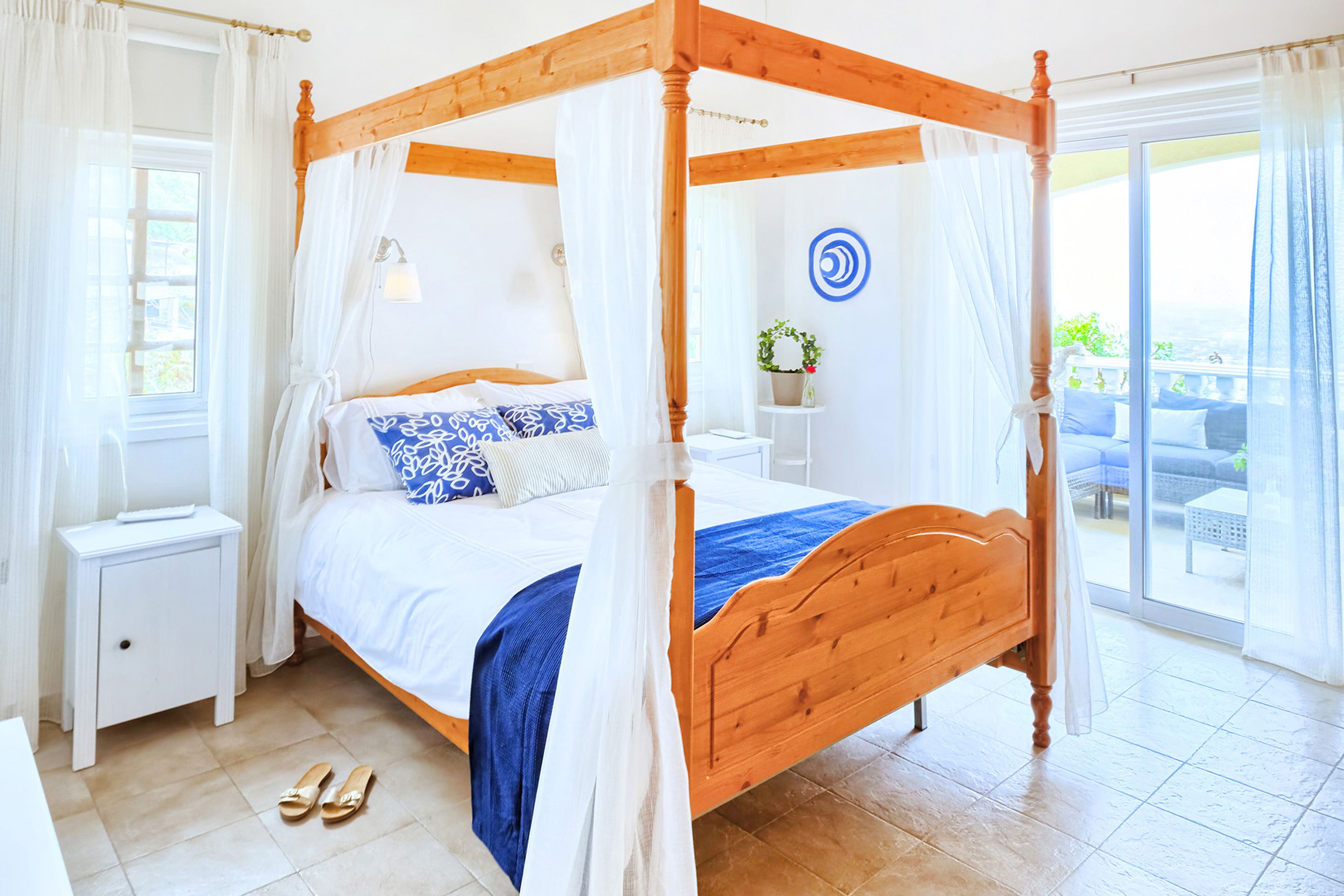 Uma cama com dossel e cortinas, uma mesinha de cabeceira e vista para a área externa.
