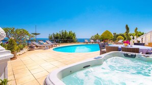 A swimming pool with lounge chairs and a hot tub, surrounded by potted plants and a view of the sea. - Villa Captains (Pegeia)