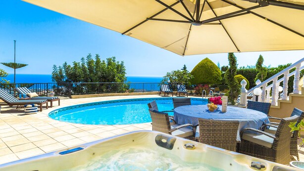 A pool area with a hot tub, lounge chairs, and a table with umbrellas. - Villa Captains (Pegeia)