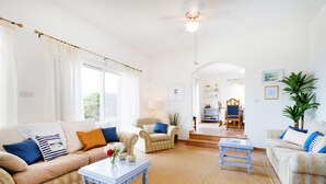 A spacious living room with a beige sofa, a coffee table, and a dining area in the background. - Villa Captains (Pegeia)