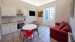 Una cocina compacta con zona de comedor, un sofá rojo y un suelo estampado.