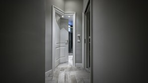 Un pasillo con una puerta que da a un baño, un interruptor de luz y suelo de baldosas.