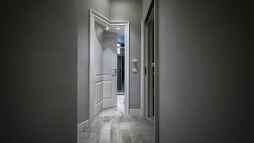 Un pasillo con una puerta que da a un baño, un interruptor de luz y suelo de baldosas.