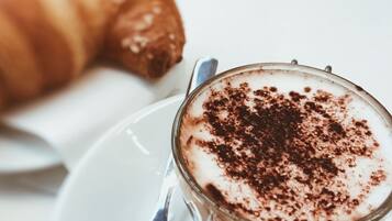 Una taza de café con espuma y un poco de cacao en polvo, junto a un croissant sobre un plato blanco.