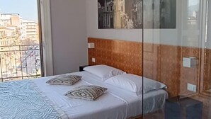 Un dormitorio con cama, un ventanal grande, vista a la ciudad y un cuadro en la pared.