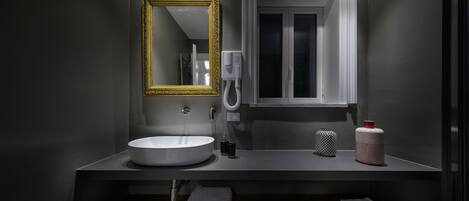 A modern bathroom with a white sink, a gold-framed mirror, a white toilet, and a window.