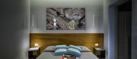 Un dormitorio moderno con una cama grande, dos mesitas de noche, cabecera de madera y una obra de arte con motivos urbanos en la pared.