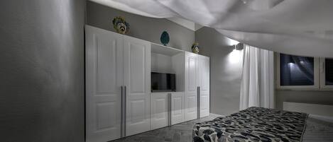 A bedroom with a large wardrobe, a bed with a patterned cover, and a window with curtains.