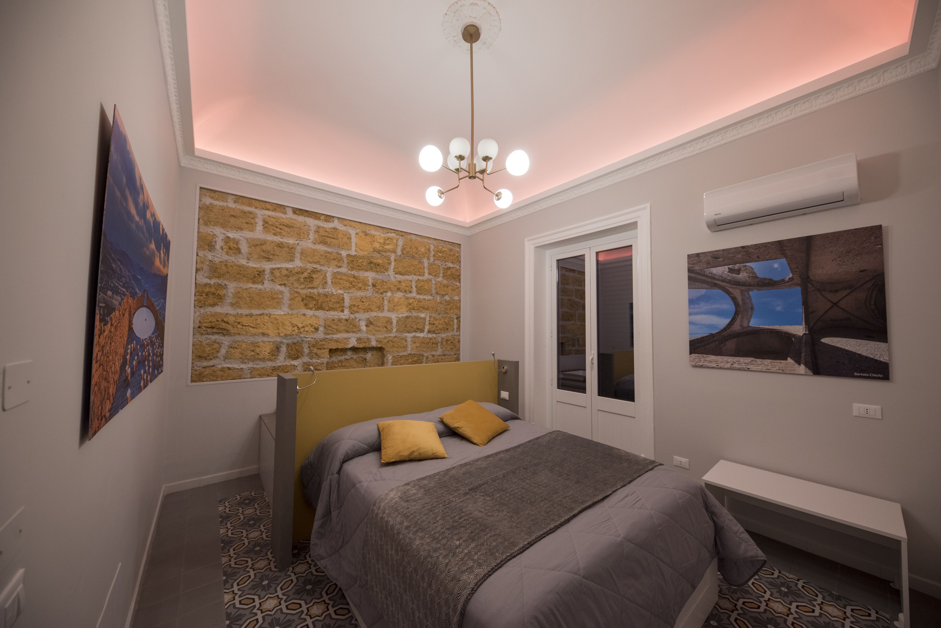 A bedroom with a brick wall, a bed with a headboard, a bedside table, and a ceiling light fixture.