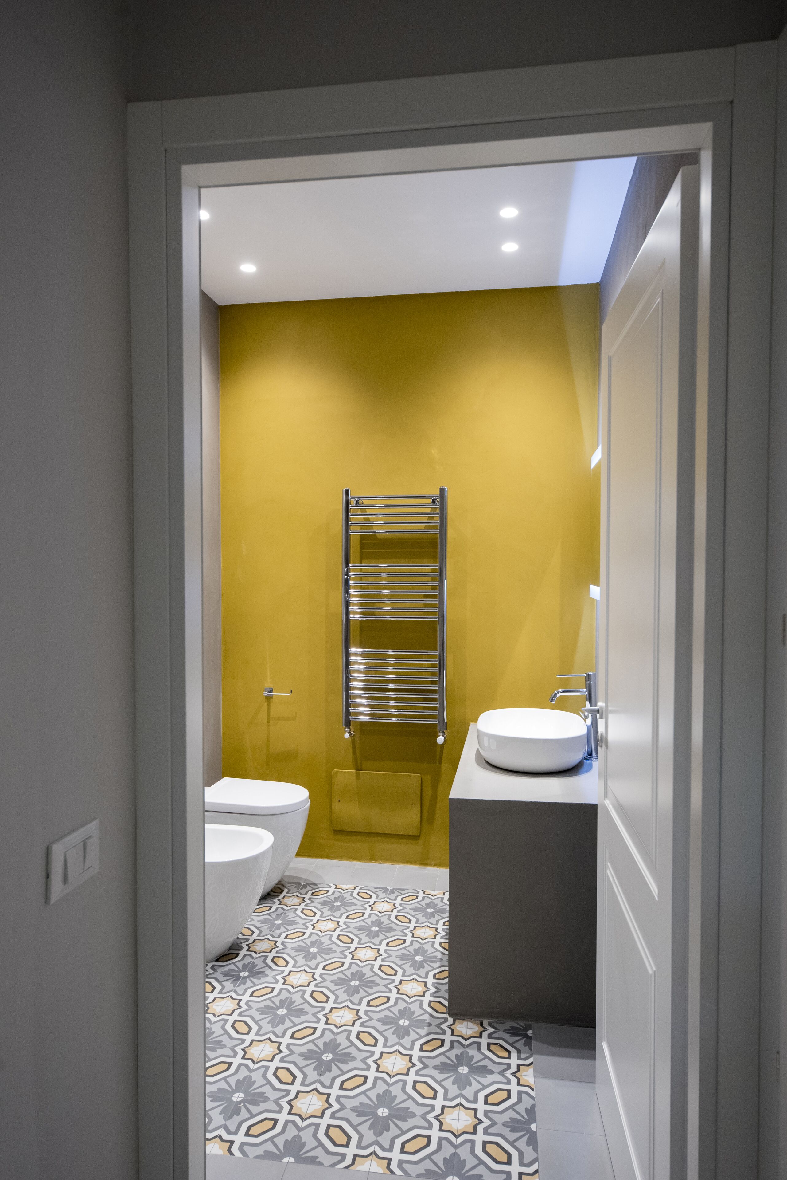 A bathroom with a yellow wall, a white sink, and a patterned floor.