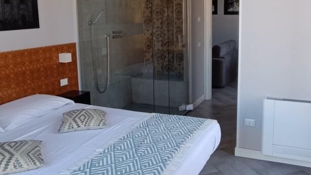 A modern hotel room with a large bed, a shower area, and a view of the city. - Suite del Ponte Normanno (Palermo)
