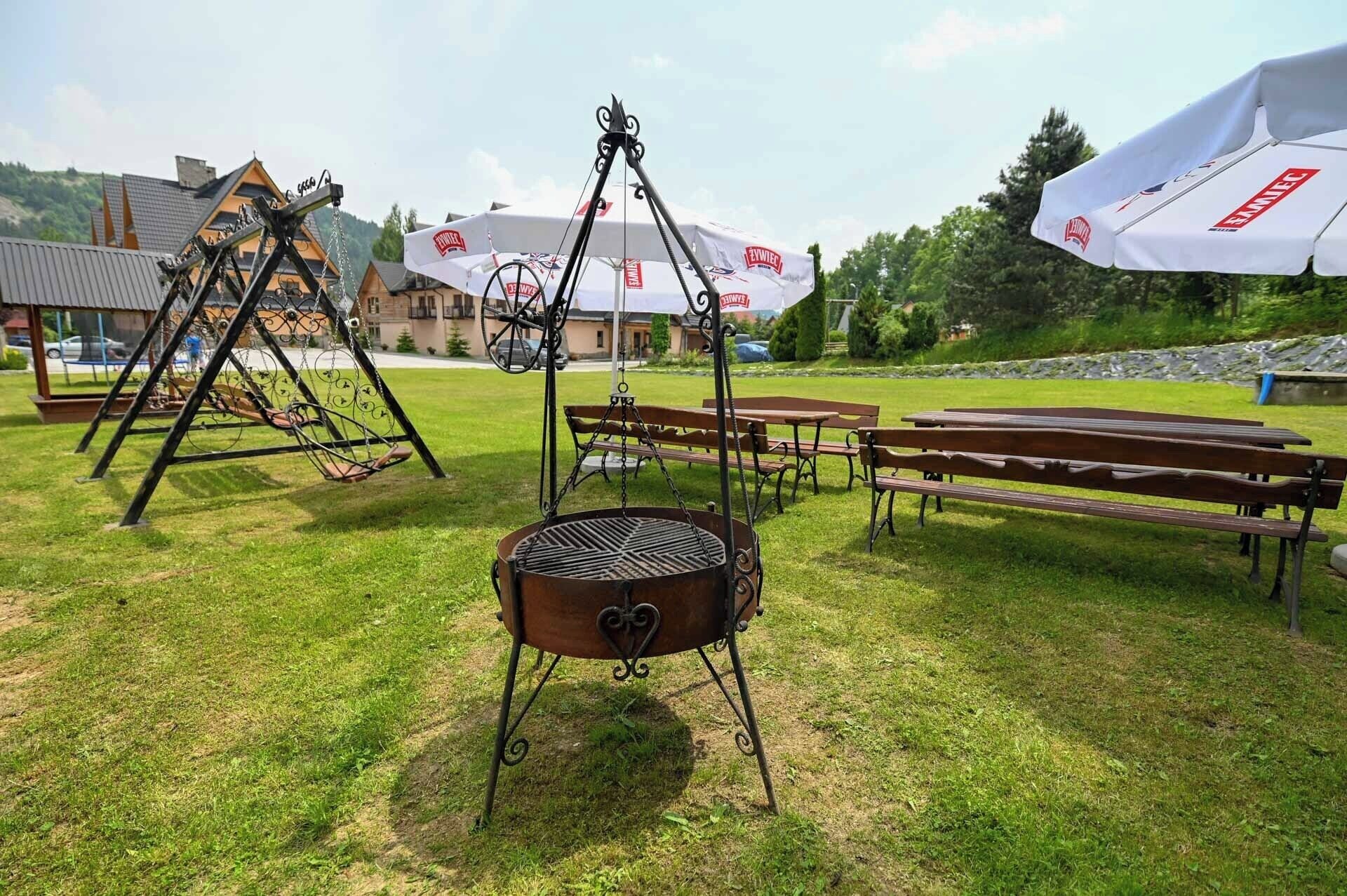 Una parrilla, mesas de picnic y un conjunto de columpios en un espacio al aire libre cubierto de césped.