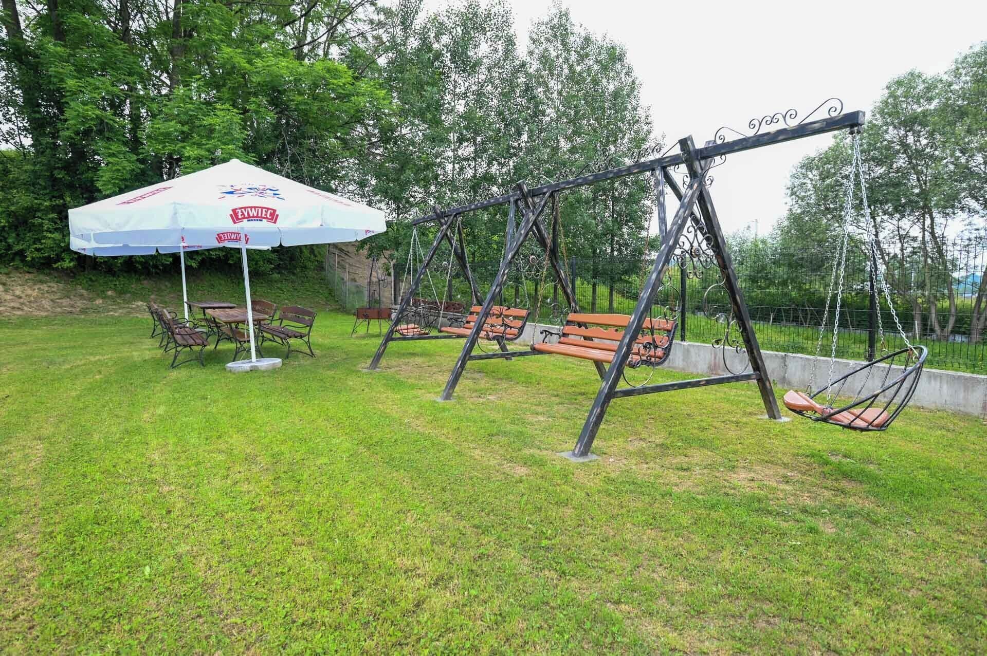 Une structure de jeux avec des balançoires, des bancs, une table de pique-nique et un espace abrité orné d’un logo.