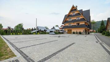 A building with a sloped roof, a parking area with a cobblestone pattern, and a few cars parked.