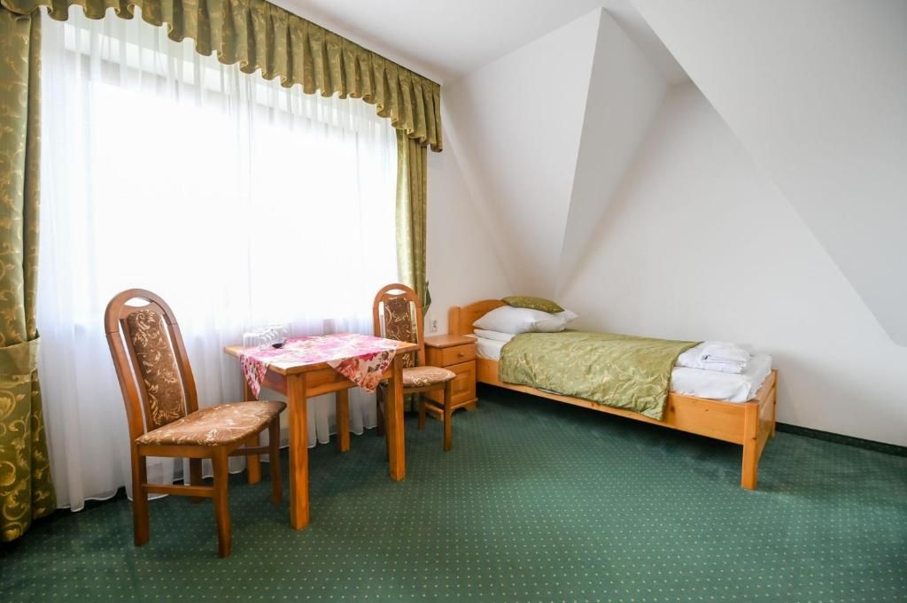 A bedroom with a bed, a desk, two chairs, and a window with curtains.