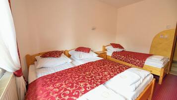 Ein Zimmer mit zwei Einzelbetten, beide mit Holz-Kopfteilen, weißer Bettwäsche und Decken mit rotem und goldenem Muster. An der Wand befindet sich ein Holzschrank und ein Heizkörper.