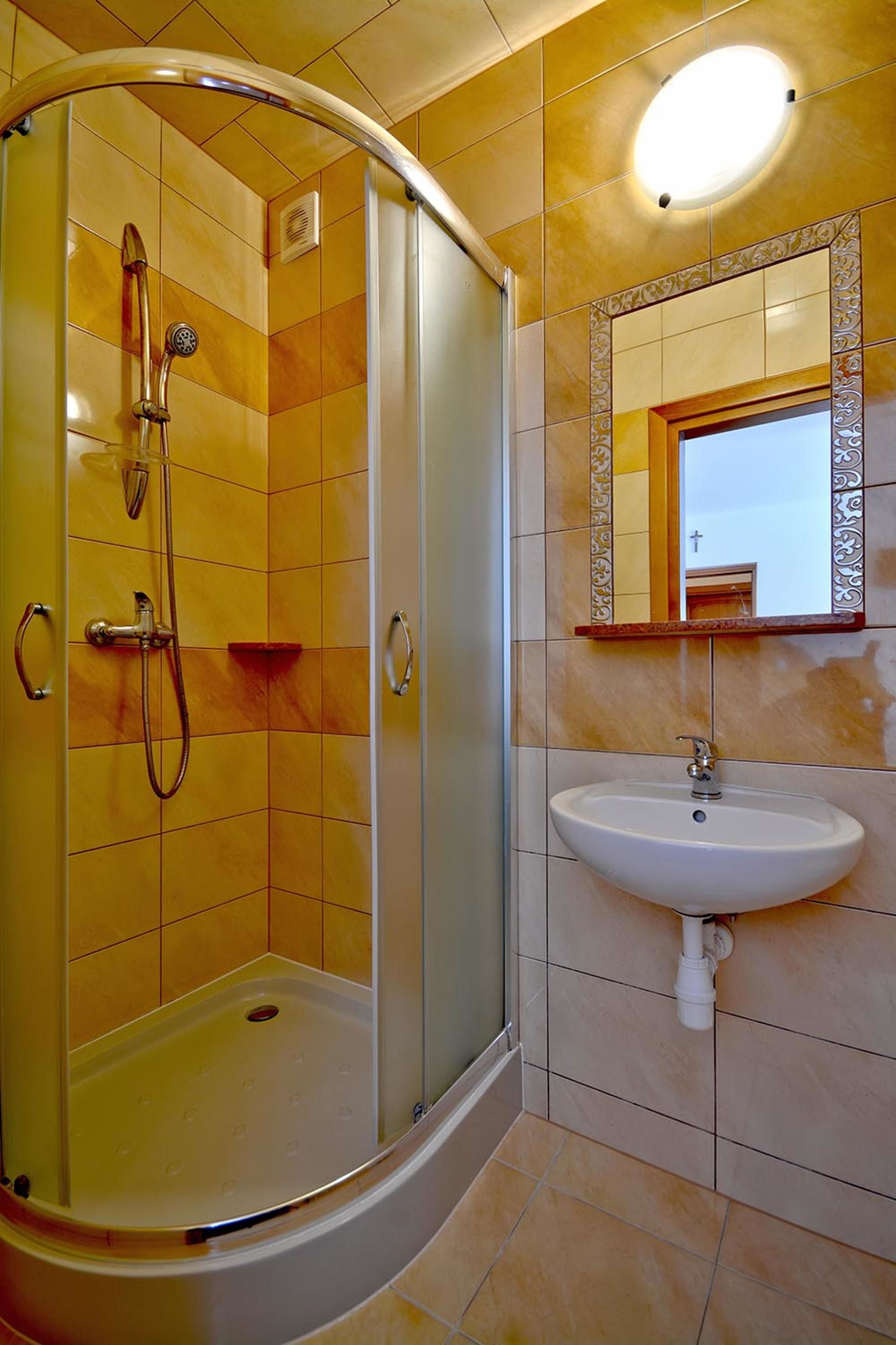 A bathroom with a glass-enclosed shower, a sink, and a mirror with a decorative frame.