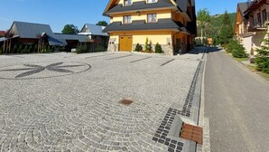 Un edificio de varios pisos con techo inclinado, un patio empedrado y un cielo azul despejado.