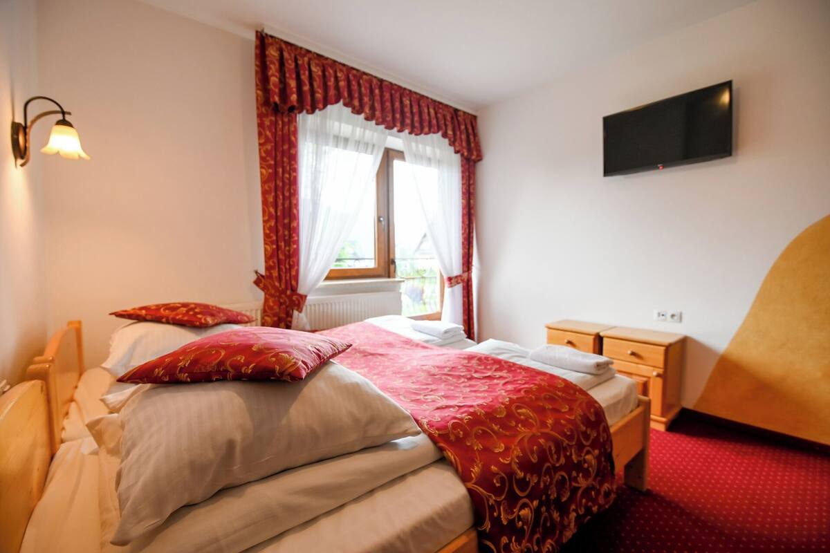Une chambre à coucher comprenant un lit, une table de chevet, un téléviseur fixé au mur et une fenêtre avec des rideaux.