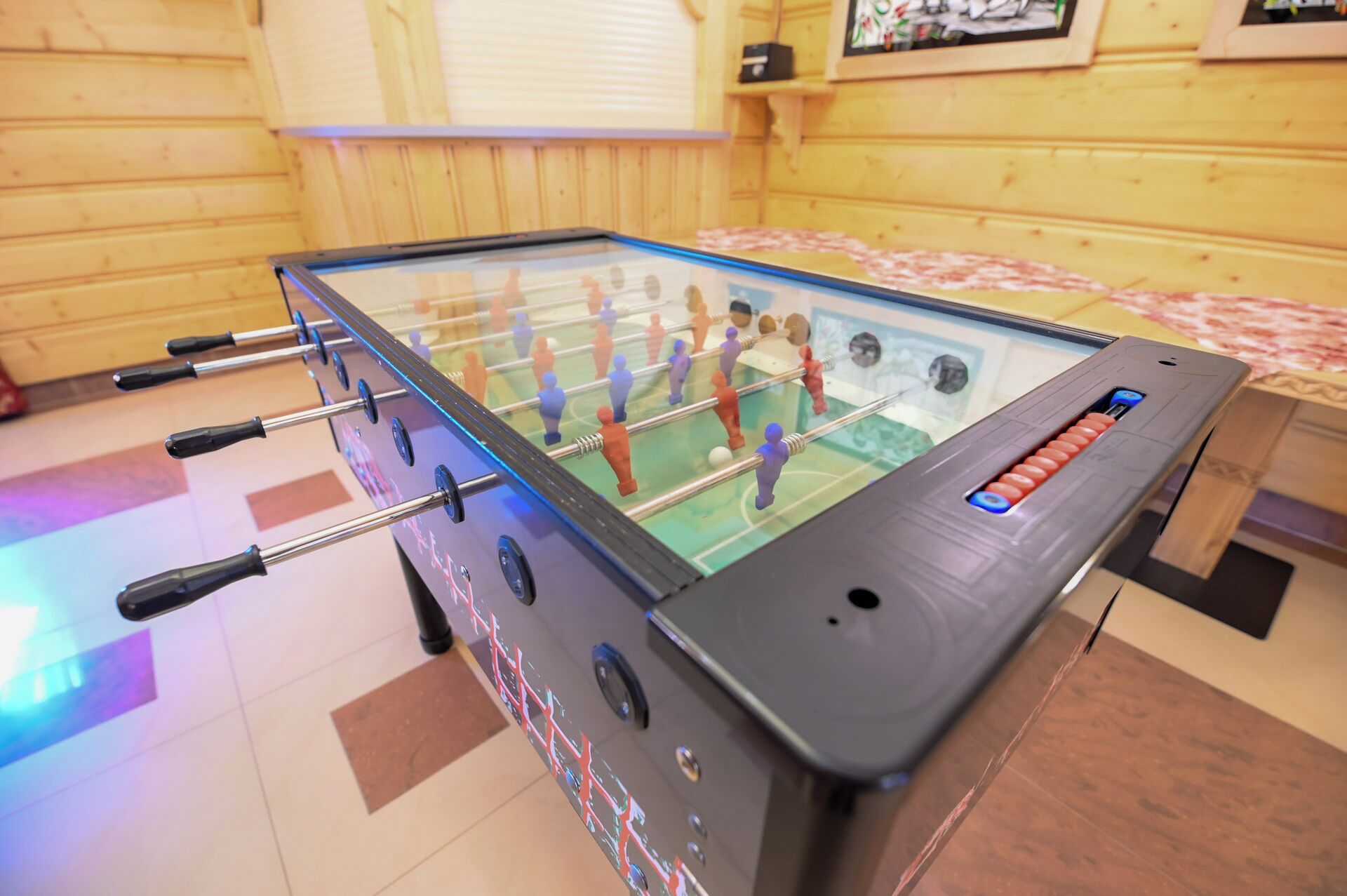 Une table de baby-foot dans une pièce aux murs en bois et un lit recouvert d’une couvre-lit à motifs floraux.