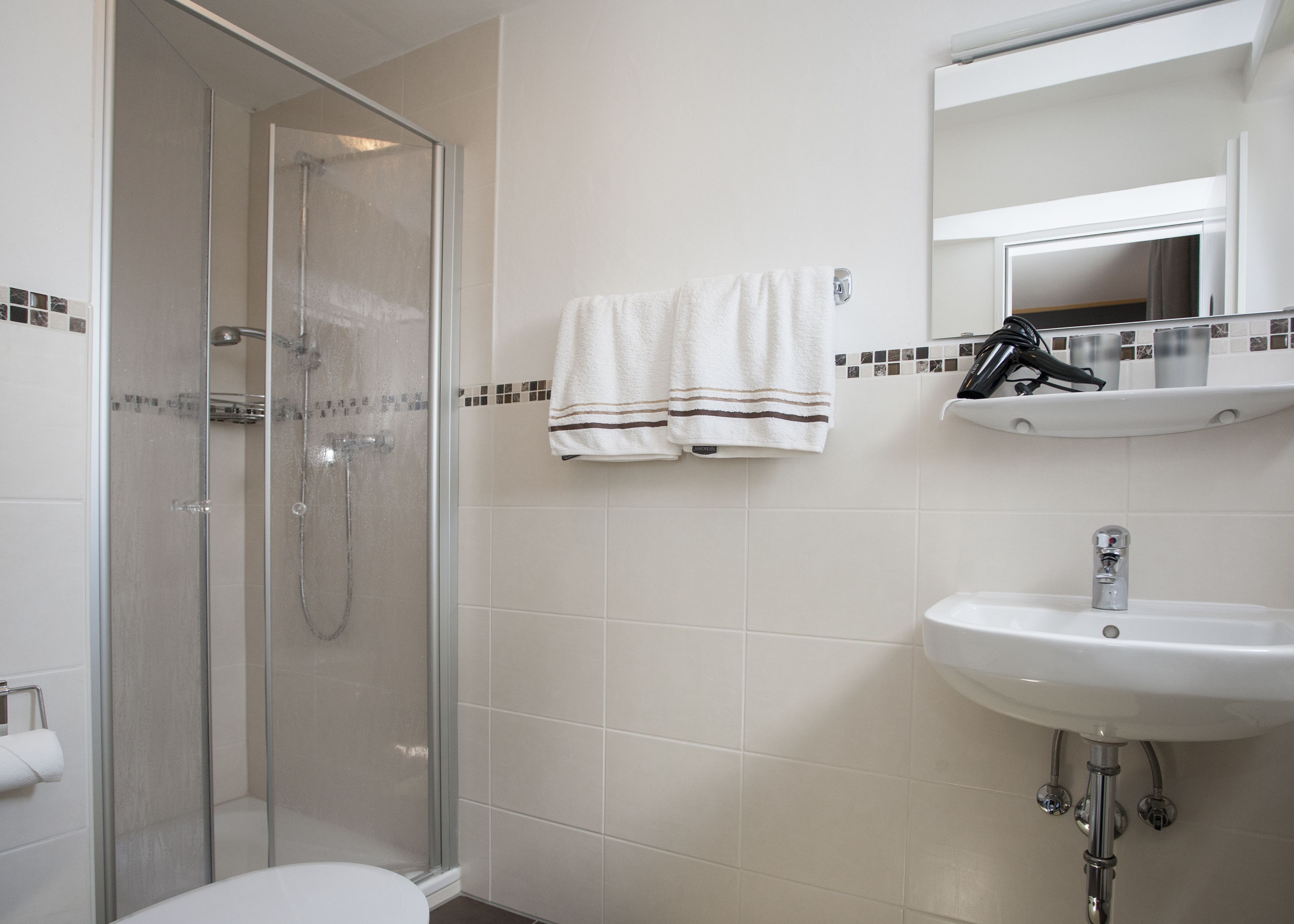 A bathroom with a glass-enclosed shower, a sink, and a mirror above it.