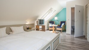 A hotel room with a large bed, a television, a desk with a lamp, two wicker chairs, and a bathroom visible through an open door. - Pension Haus Brieden (Winterberg)